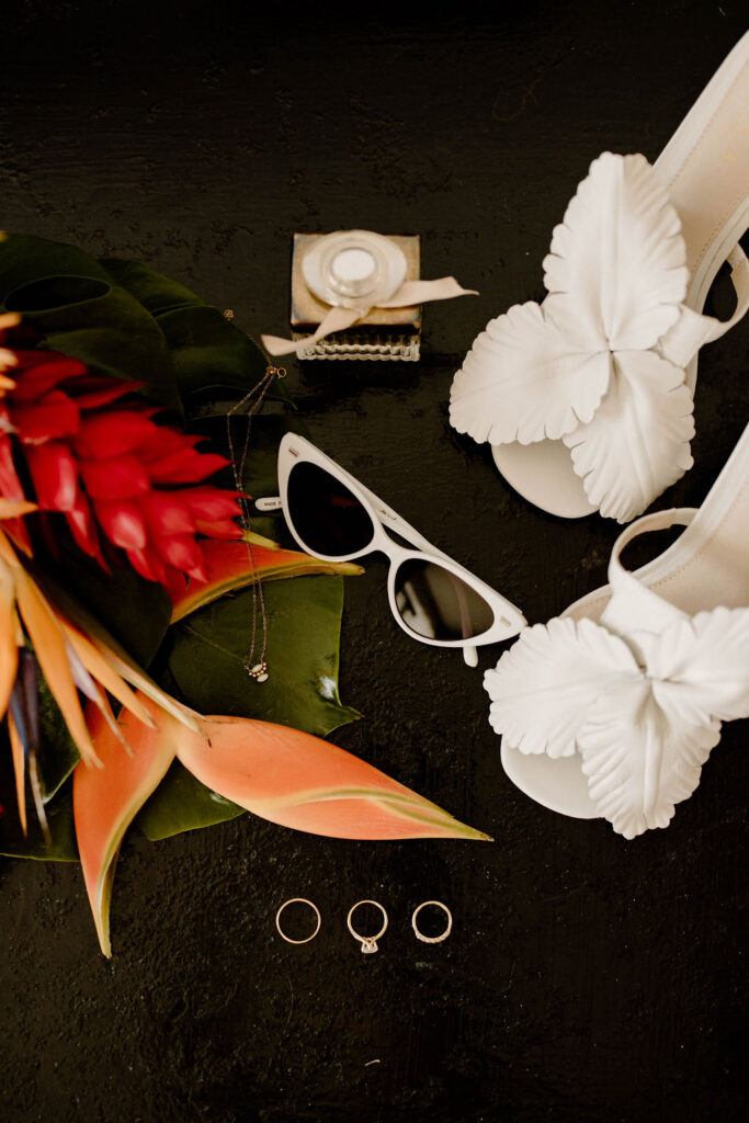 Bridal wedding details including white floral heels, rings, tropical flowers, and accessories at Majestic Elegance Costa Mujeres.
