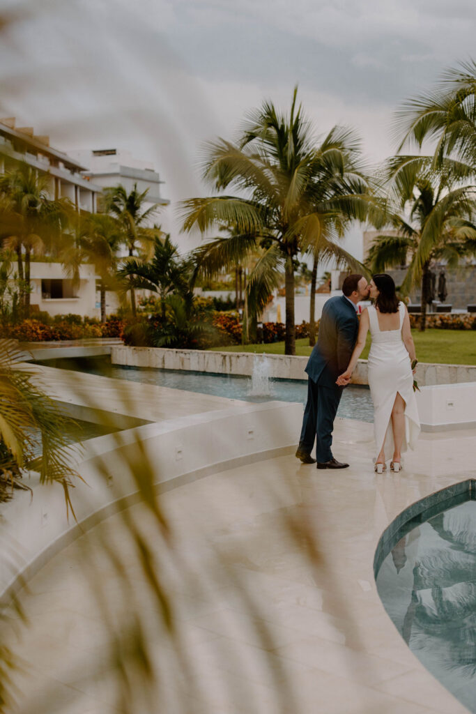 Newlywed couple sharing a kiss beside the pools and tropical gardens at Majestic Elegance Costa Mujeres.