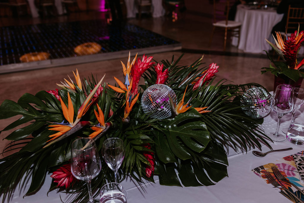 Tropical wedding reception centerpiece featuring bird of paradise flowers and disco ball accents.