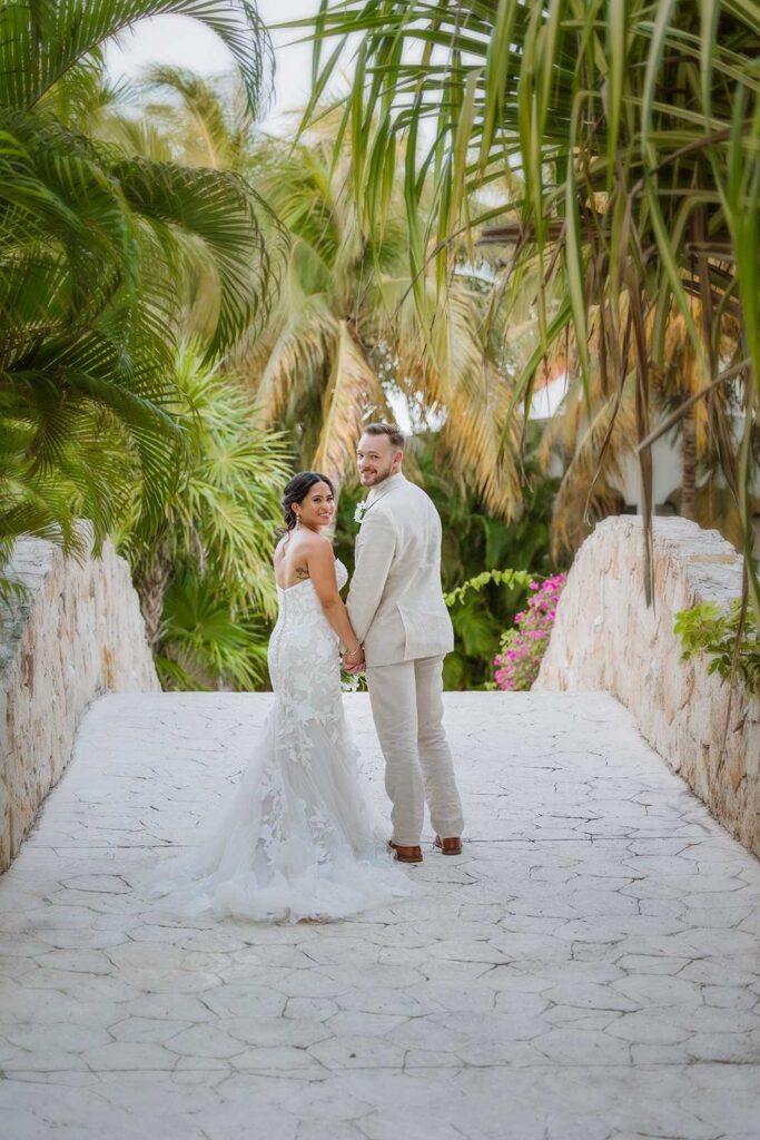 Bride and groom walking through lush tropical grounds at El Dorado Royale Resort