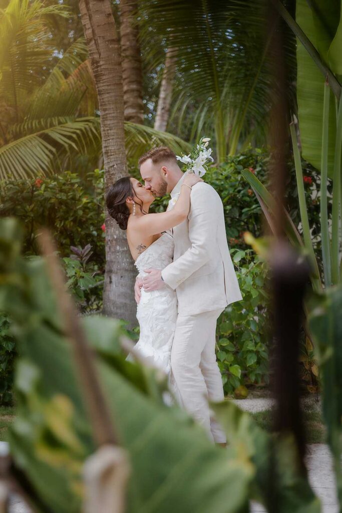 Bride and groom kissing among tropical palm trees and gardens in Riviera Maya