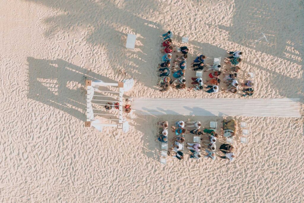 Aerial view of a beachfront wedding ceremony setup at Secrets Maroma Beach Riviera Cancun with guests seated on white chairs along a sandy aisle.
