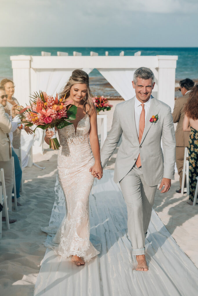 Newly married couple walking down the aisle after their beach wedding ceremony at Secrets Maroma Beach Riviera Cancun.