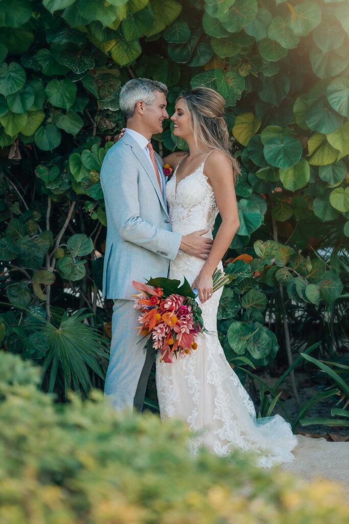 Bride and groom embracing among tropical greenery after their wedding at Secrets Maroma Beach Riviera Cancun.