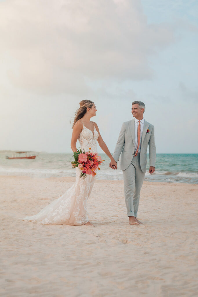Bride and groom walk hand in hand along the beach at Secrets Maroma Beach Riviera Cancun after their destination wedding ceremony.