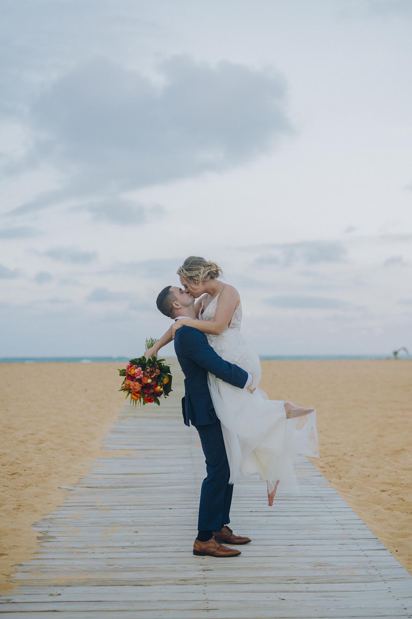 Couple kissing on a pathway to the beach, showing ​who is an expert destination wedding travel agent