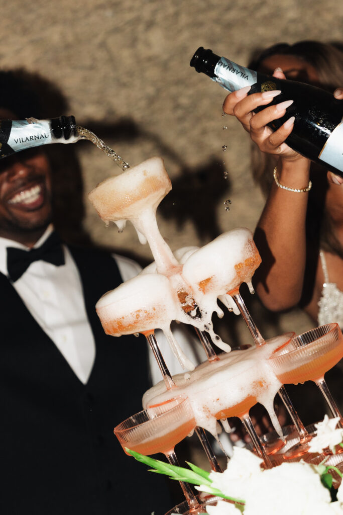 Couple pouring champagne over a champagne tower during a luxury mexico destination wedding reception.