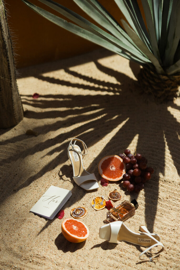 Beach wedding detail flat lay featuring bridal heels, perfume, citrus, and tropical styling.