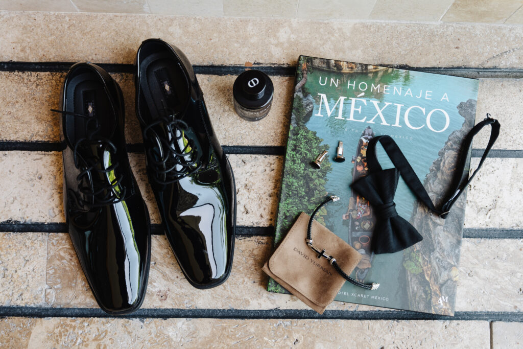 Groom wedding details featuring black patent dress shoes, bow tie, cufflinks, cologne, and accessories for a luxury destination wedding in Mexico.
