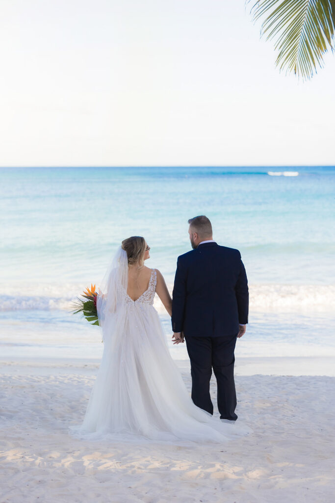 Bride and groom walking hand in hand along a white sand beach after their destination wedding ceremony.